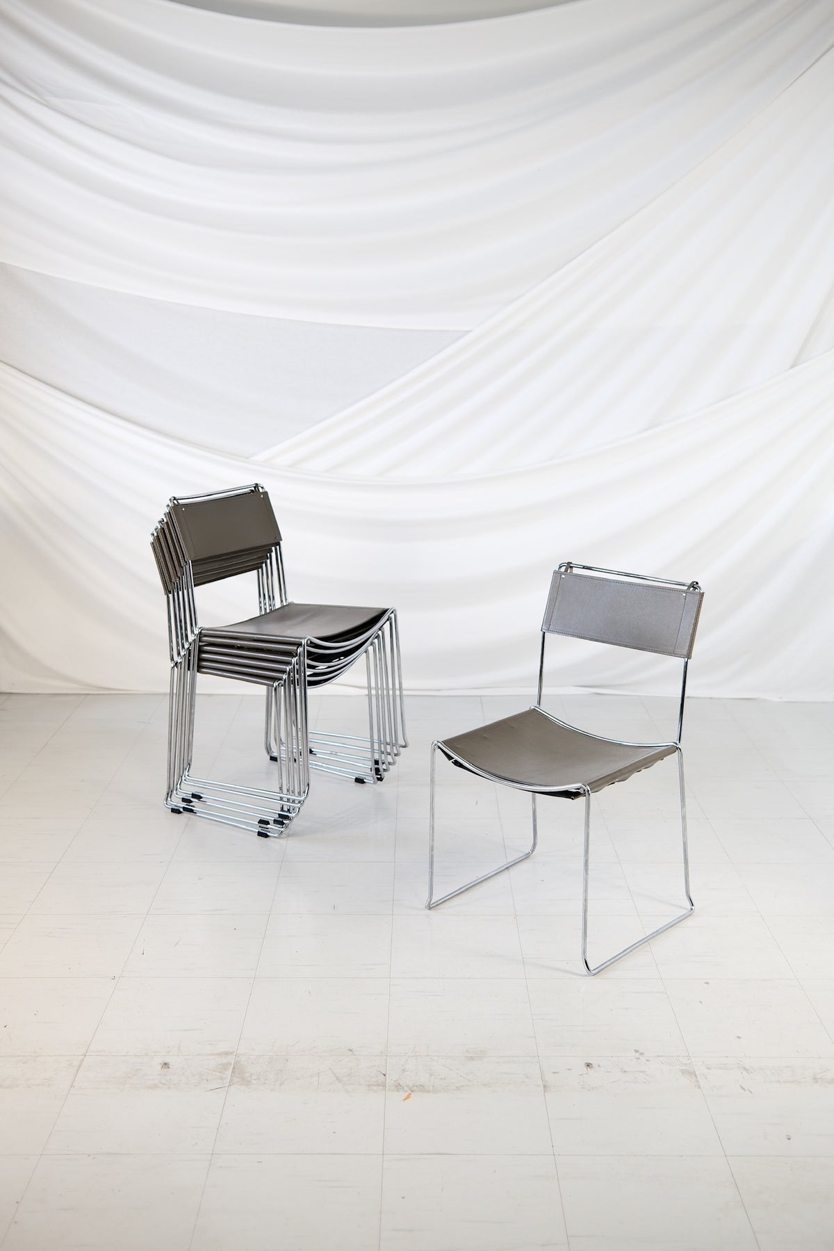 Set med 7 italienska vintagematstolar med kromstomme och sits och rygg i grått läder, stapelbar modell.